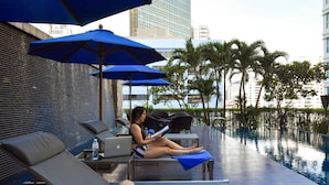 A poolside area with lounge chairs, umbrellas, and a laptop on a table. - Hilton Bangkok Grande Asoke (Bangkok)