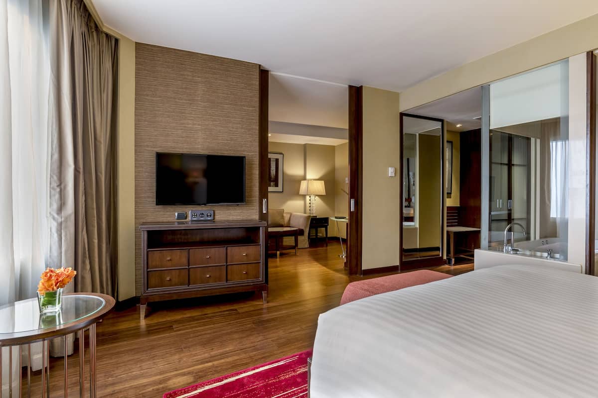 Een hotelkamer met een groot bed, een televisie op een houten standaard, een bureau met een lamp en een badkamer zichtbaar door een geopende deur.