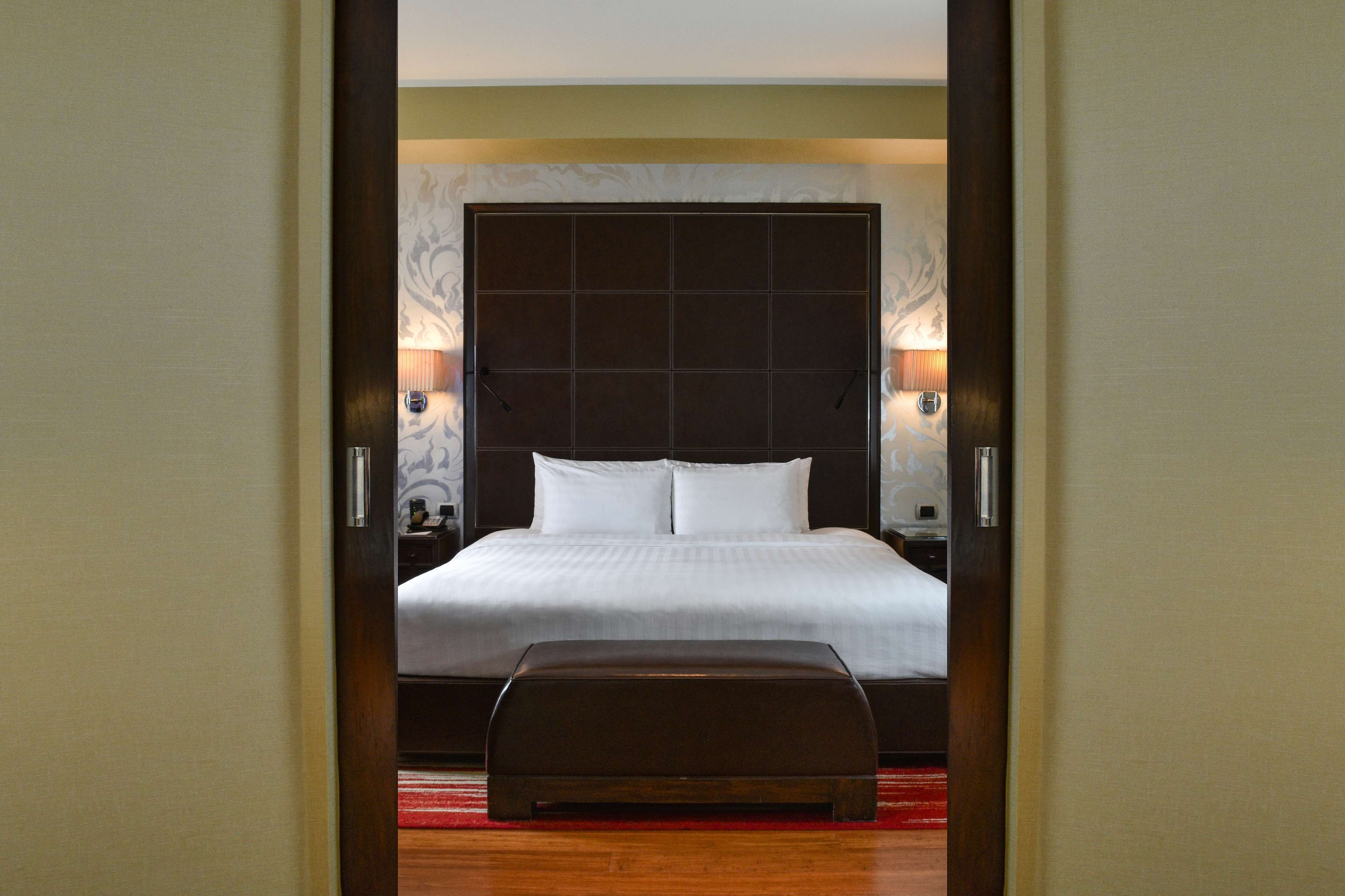 Ein Hotelzimmer mit einem großen Bett, einer hölzernen Bank und einem Nachttisch mit einer Lampe.