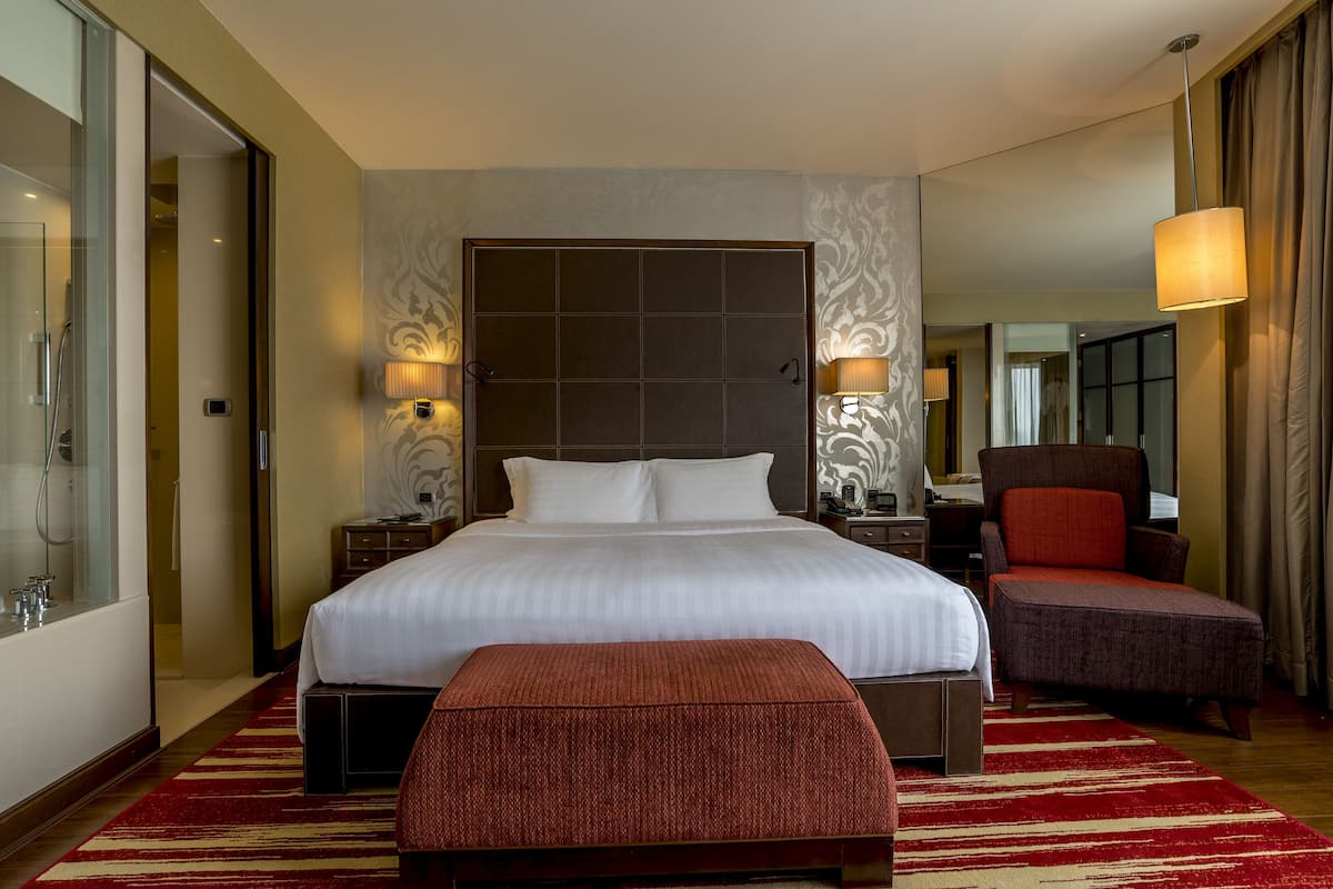 Een hotelkamer met een groot bed, een rode gestoffeerde bank, een stoel, een nachtkastje en een lamp.