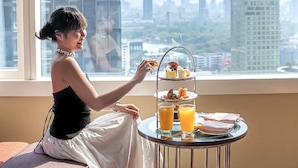 A person sitting by a window with a three-tiered dessert stand and two glasses of orange juice. - Hilton Bangkok Grande Asoke (Bangkok)