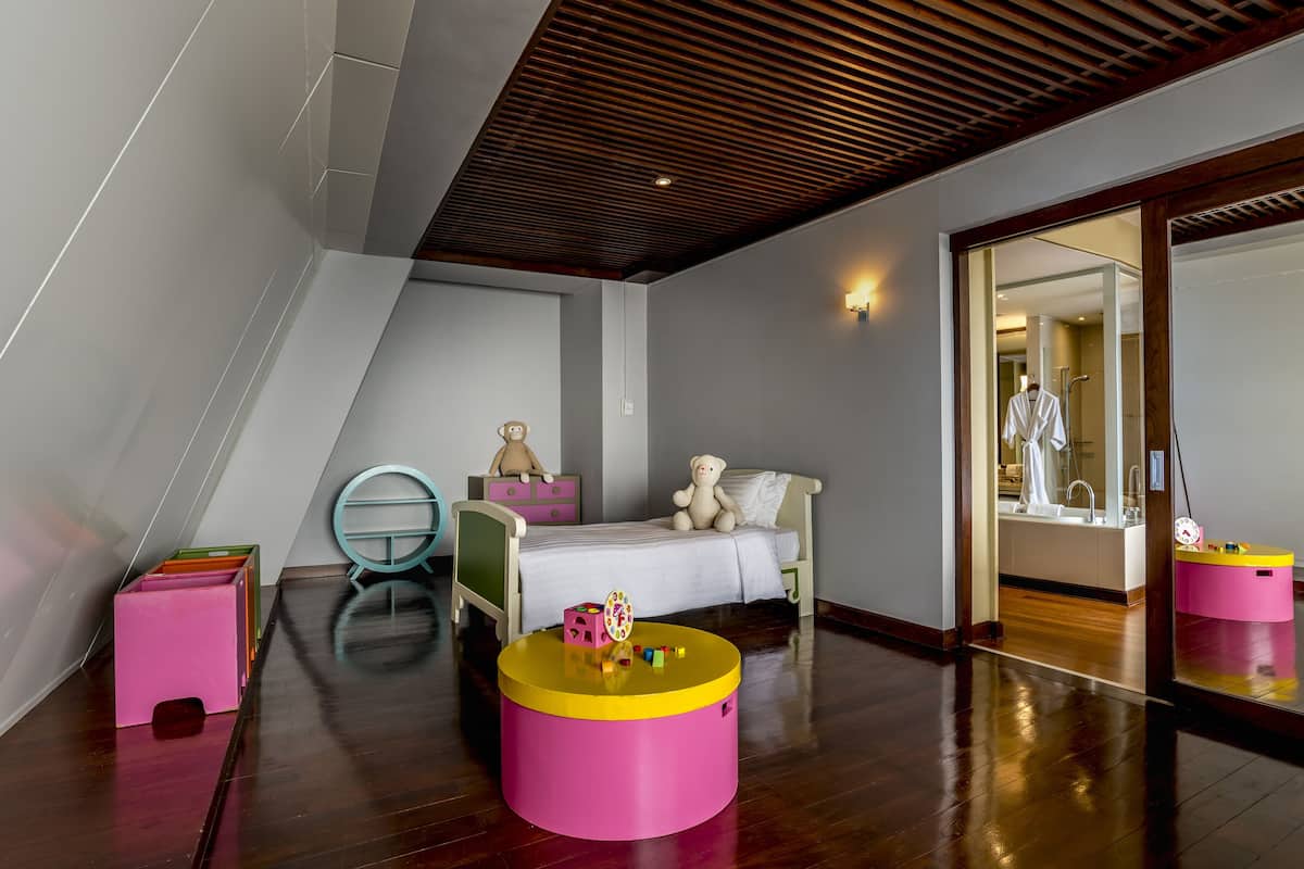 Een kinderkamer met een bed, een rond tafeltje met speelgoed, een spiegel en een houten plafond.