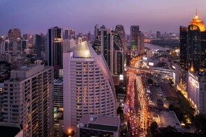 Un hotel moderno de altura con un techo curvo característico, situado en una ciudad vibrante con una calle concurrida y otros edificios altos al fondo.