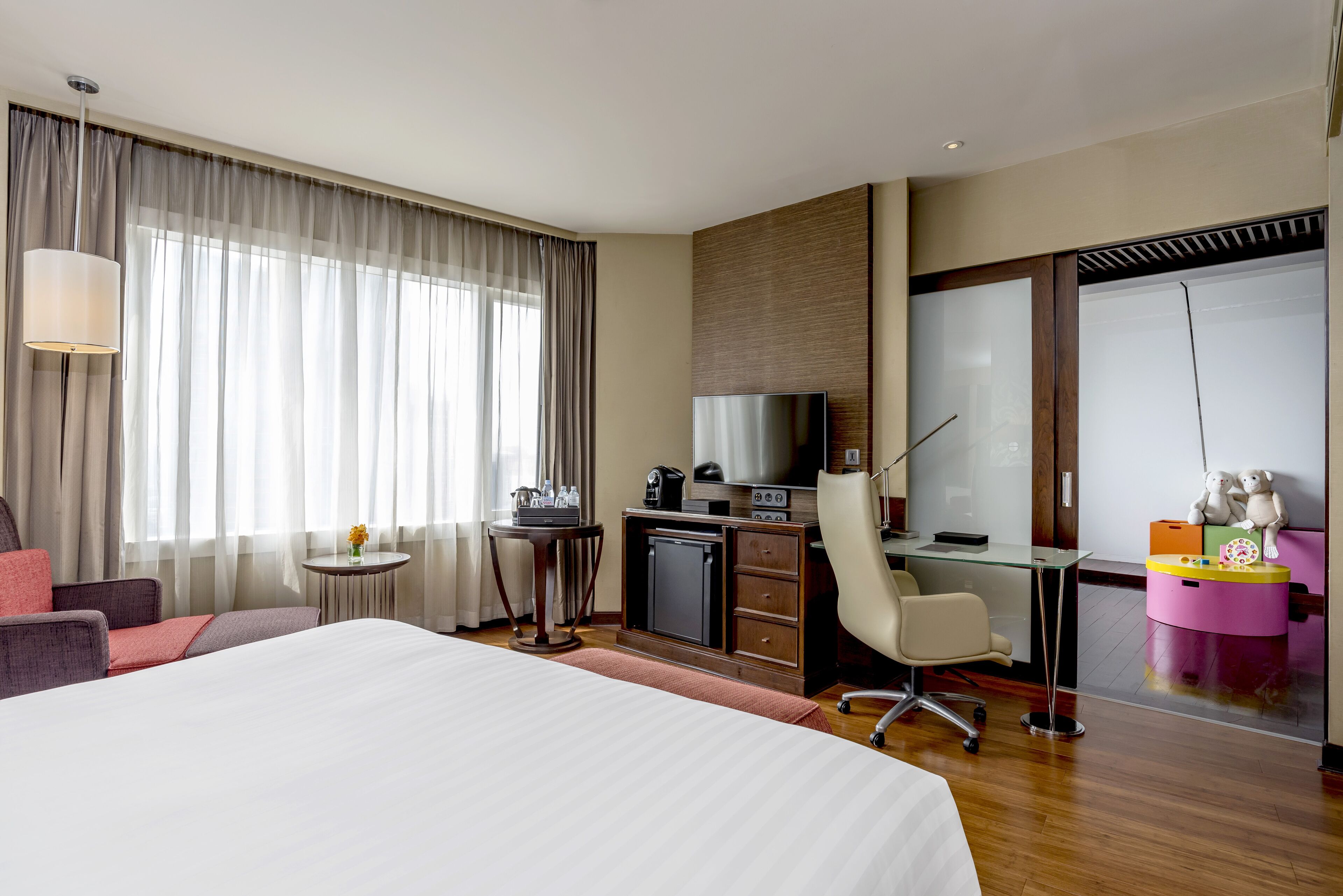 A hotel room with a large bed, a desk with a computer, a chair, a small table with a lamp, and a TV.