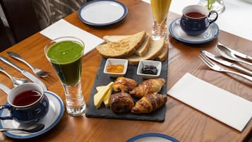 A breakfast setting with toast, croissants, jam, butter, and a green smoothie on a slate board.