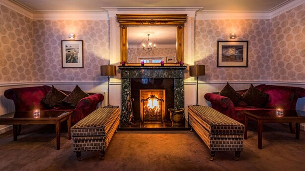 A cozy room with a fireplace, two red sofas, a brick bench, and framed pictures on the walls. - Toravaig House Hotel (Sleat)