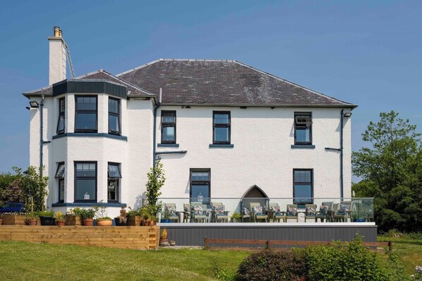 A two-story building with a balcony, a chimney, and a garden area with potted plants. - Toravaig House Hotel (Sleat)