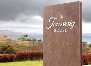 A sign for Toravaig House, a hotel and restaurant, with a scenic view of hills and a body of water in the background. - Toravaig House Hotel (Sleat)