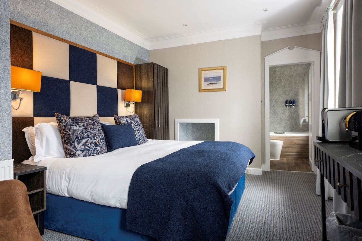 Ein Hotelzimmer mit einem großen Bett, einem Schreibtisch und einem durch eine offene Tür einsehbaren Badezimmer.