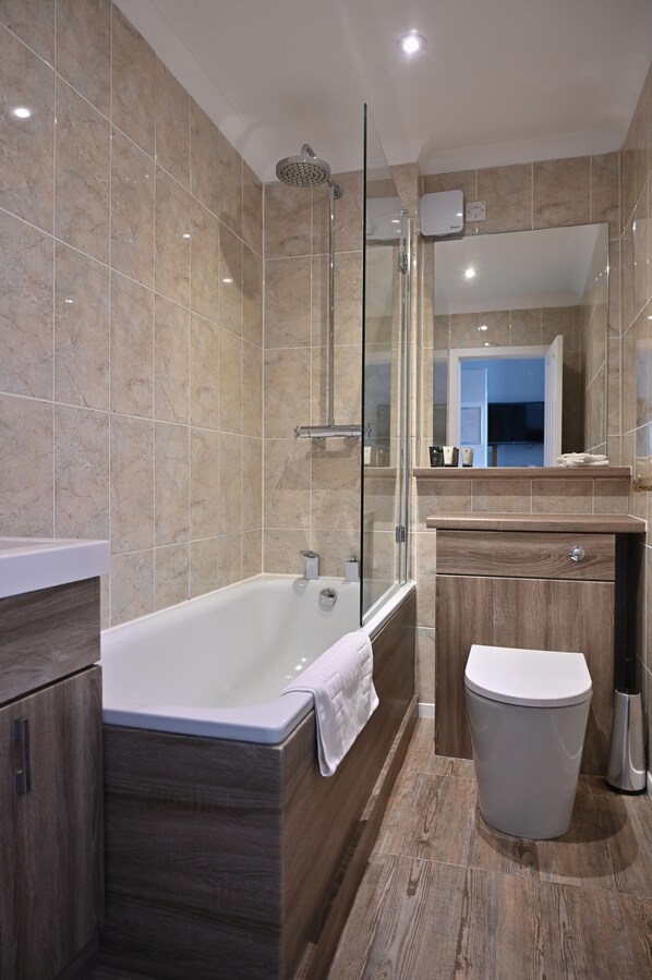 Une salle de bain moderne avec une douche à parois de verre, une baignoire sur pieds, un meuble-lavabo en bois et des toilettes blanches.