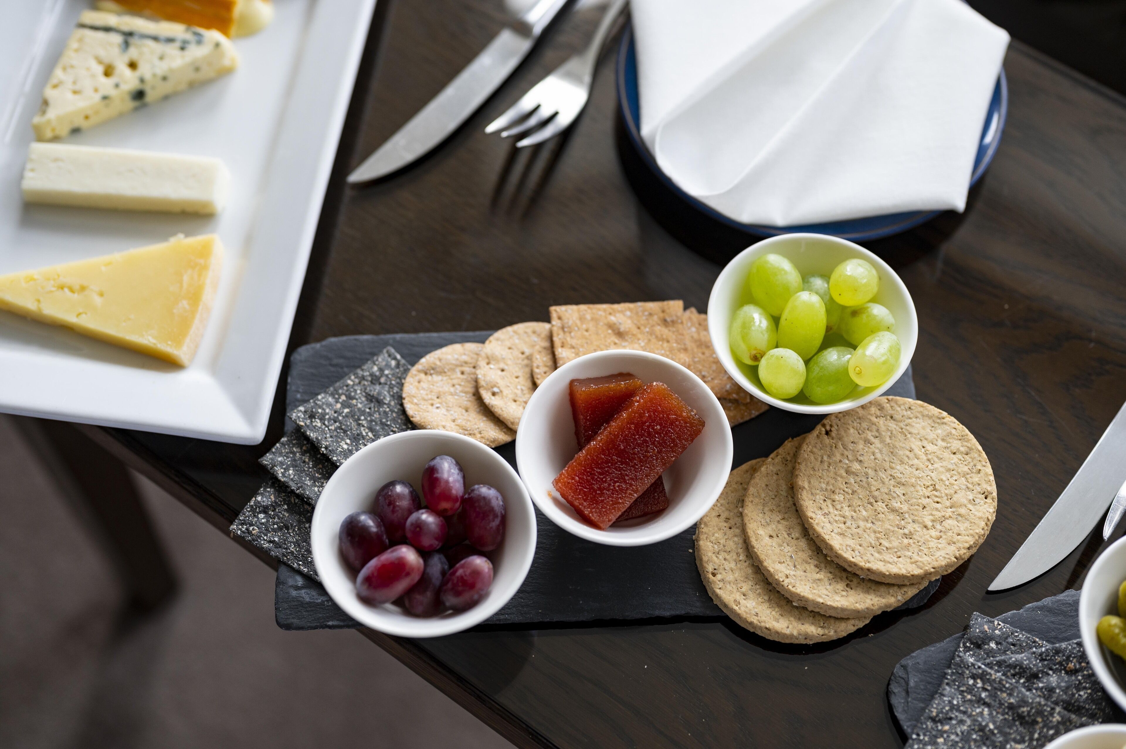 Una tabla con diversos quesos, uvas y galletas.