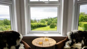 Two dogs sitting on a couch facing a window with a view of a green landscape. - Toravaig House Hotel (Sleat)