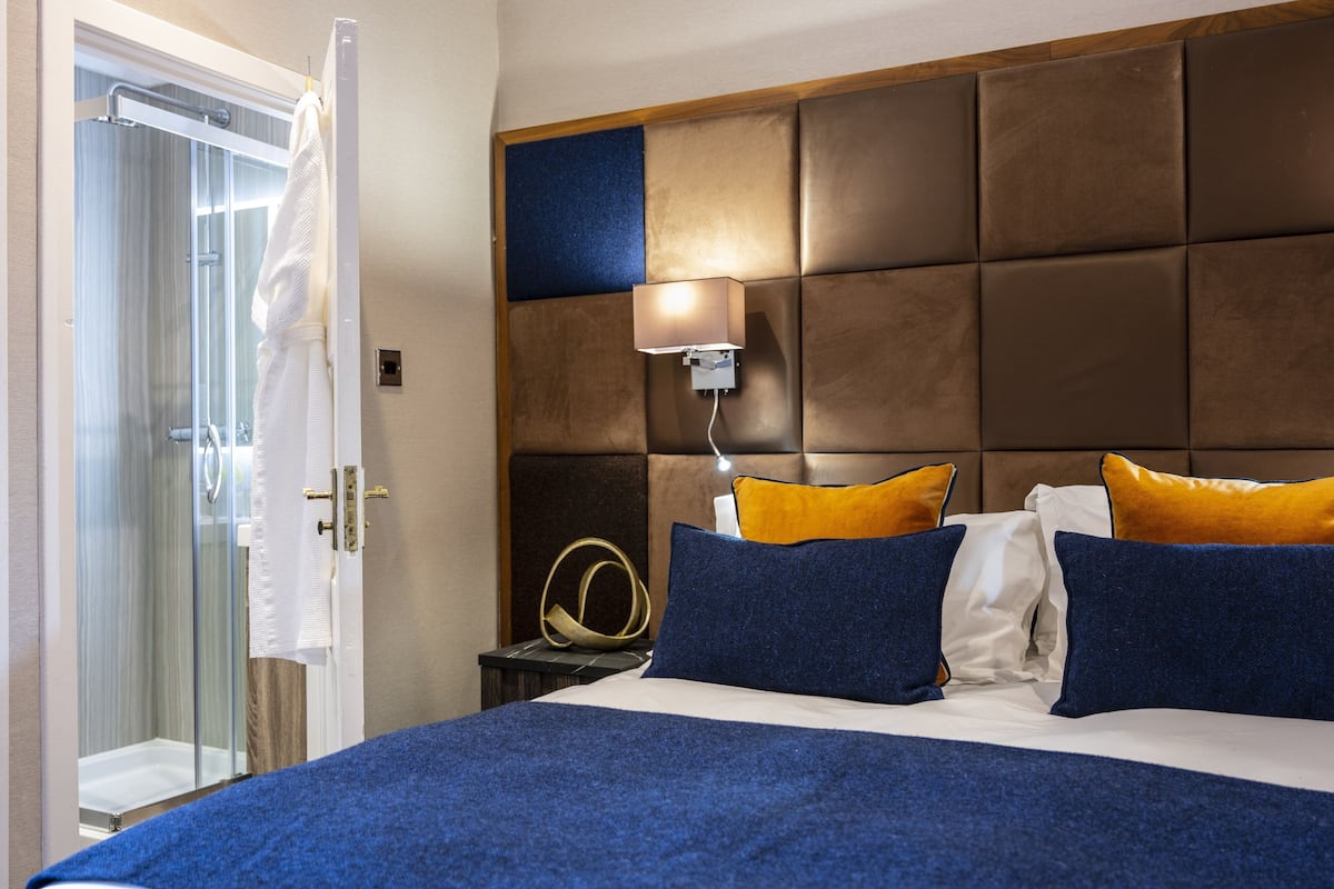 Ein Hotelzimmer mit einem Bett, einem Nachttisch, einer Lampe und einem Duschbereich.