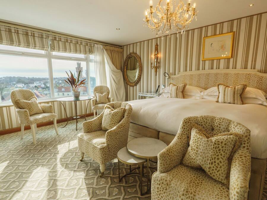 A spacious bedroom with a large bed, a chandelier, a view of the city, and leopard print furniture.