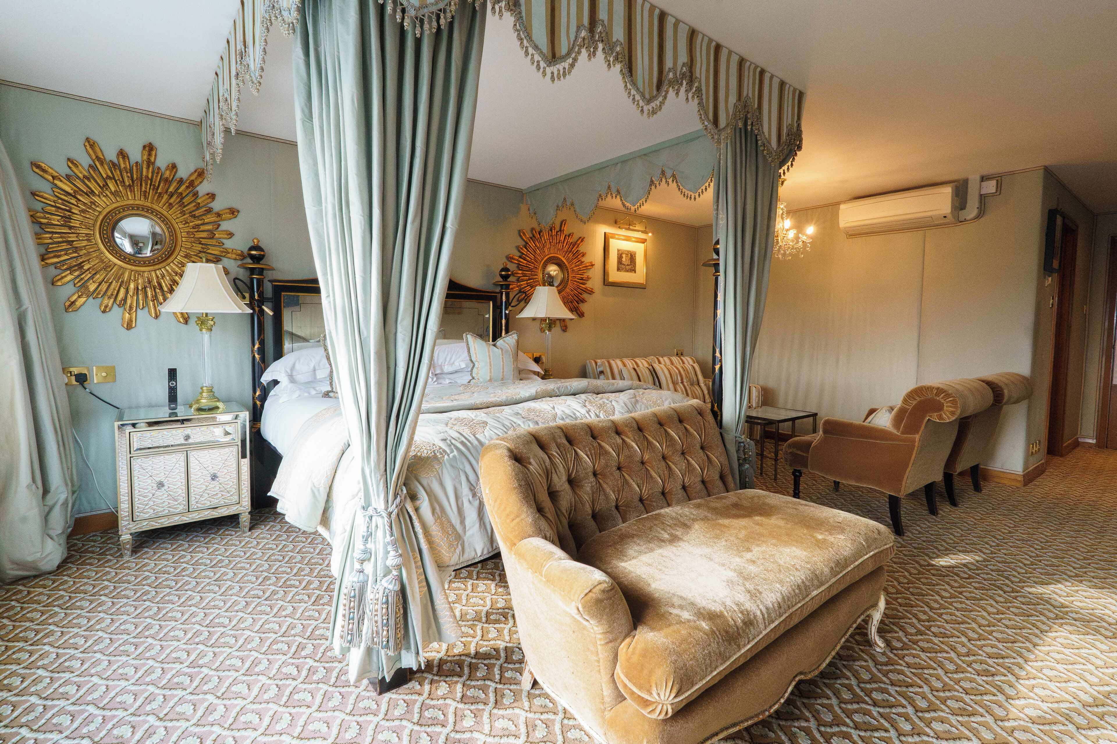 A bedroom with a four-poster bed, a tufted sofa, a nightstand, a lamp, and a mirror.