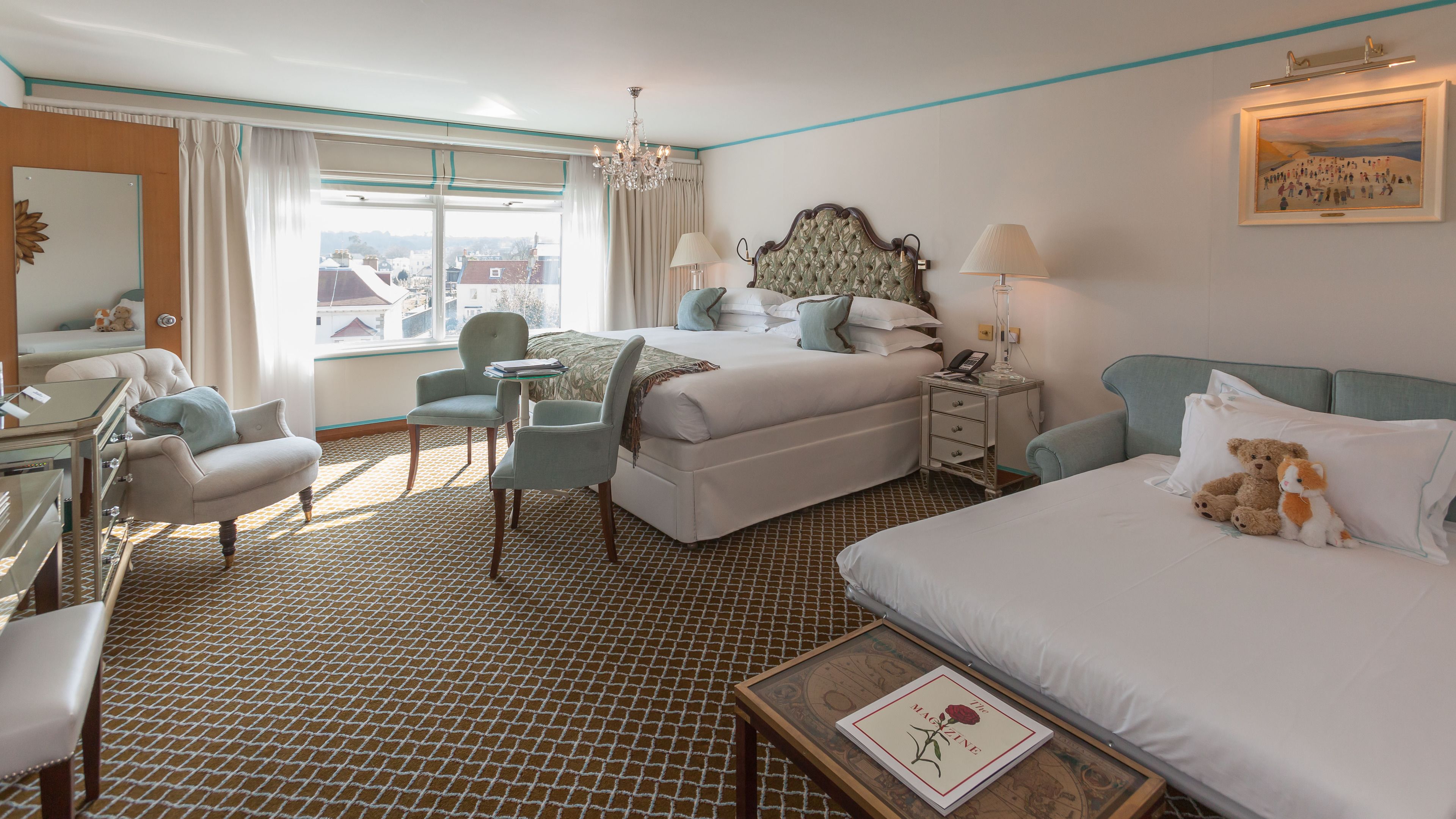 A hotel room with a large bed, two bedside tables, a desk, a chair, and a view of the city.