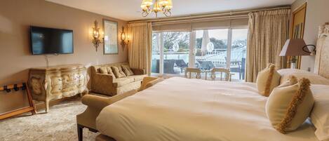 A hotel room with a large bed, a television, a dresser, and a balcony with a table and chairs.