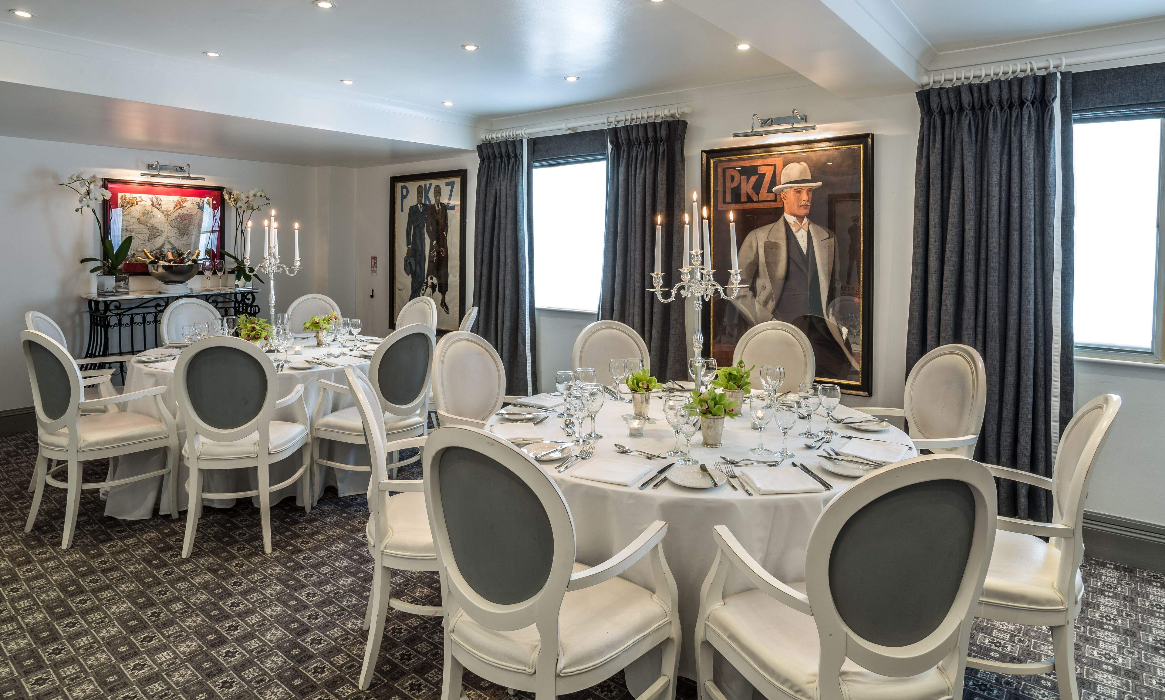 A formal dining room with round tables, white chairs, and chandeliers.