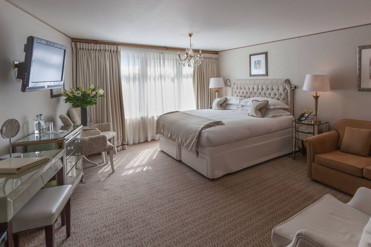Quarto de hotel com cama, área de estar com sofá, escrivaninha com espelho e TV na parede.