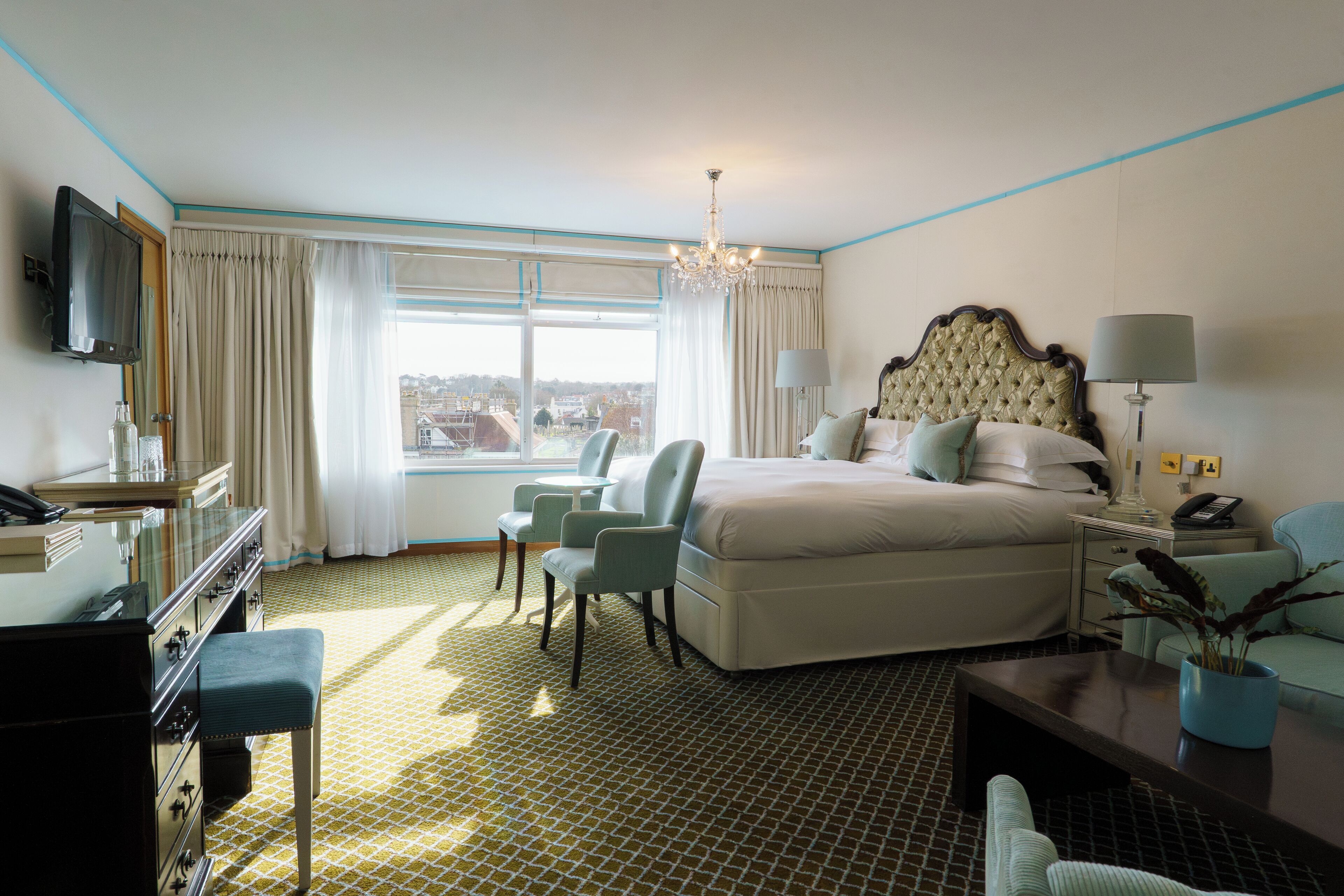 Ein Hotelzimmer mit Bett, Schreibtisch mit Lampe, Sessel, Fernseher und Blick auf die Stadt.
