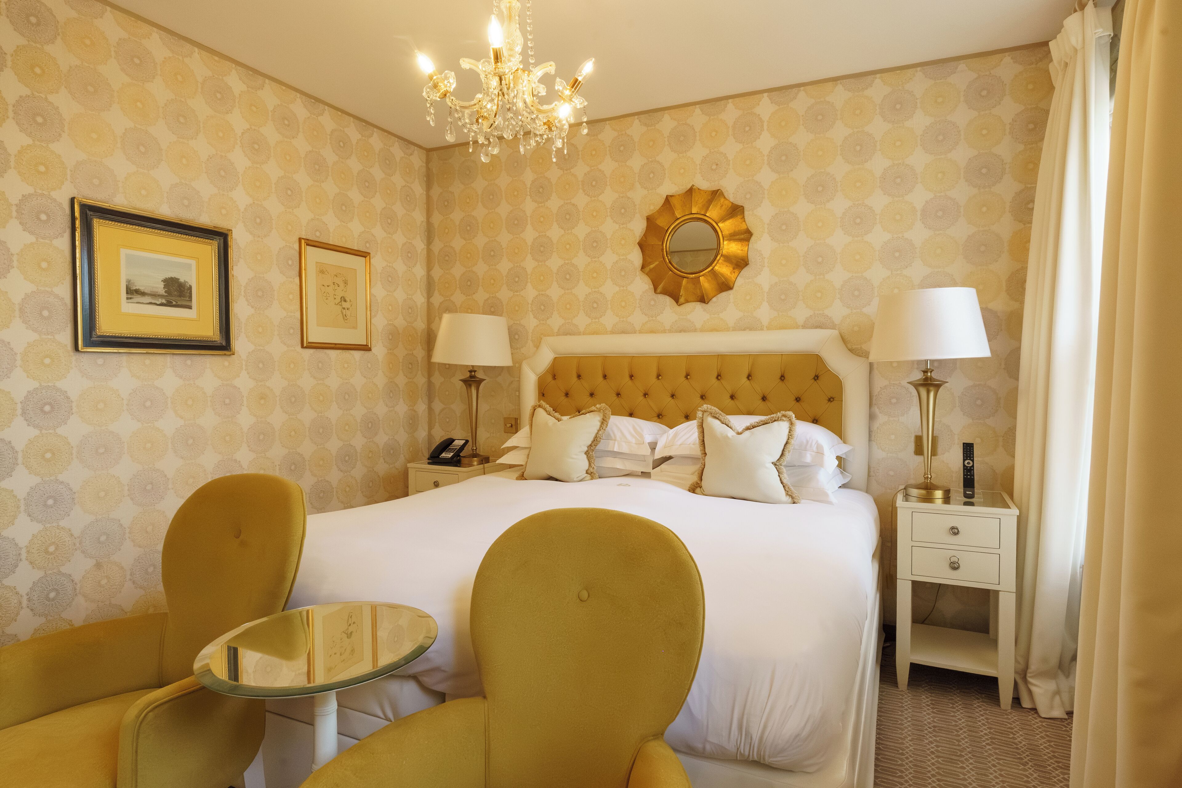 Una habitación de hotel con una cama grande, dos mesitas de noche, una araña y dos sillas.