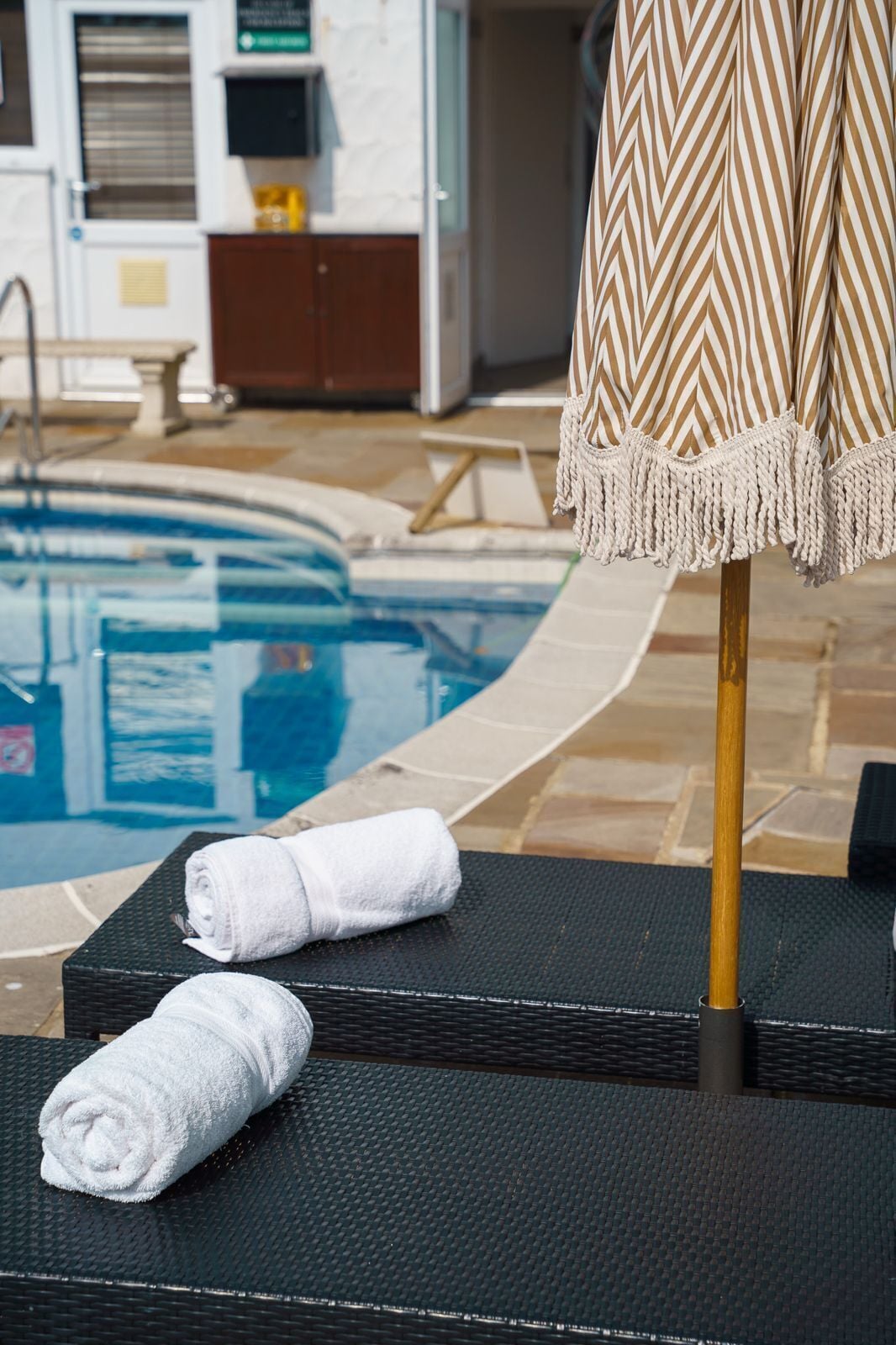 Zona junto a la piscina con una tumbona, una toalla y un parasol estampado.