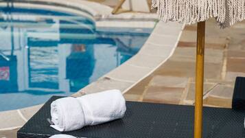 Zona junto a la piscina con una tumbona, una toalla y un parasol estampado.