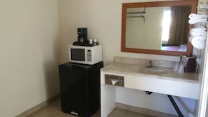 A compact bathroom with a white sink, a mirror, a microwave, and a small black refrigerator. - Vagabond Inn Hemet (Hemet)