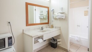A bathroom with a sink, mirror, towel rack, and a trash bin. - Vagabond Inn Hemet (Hemet)