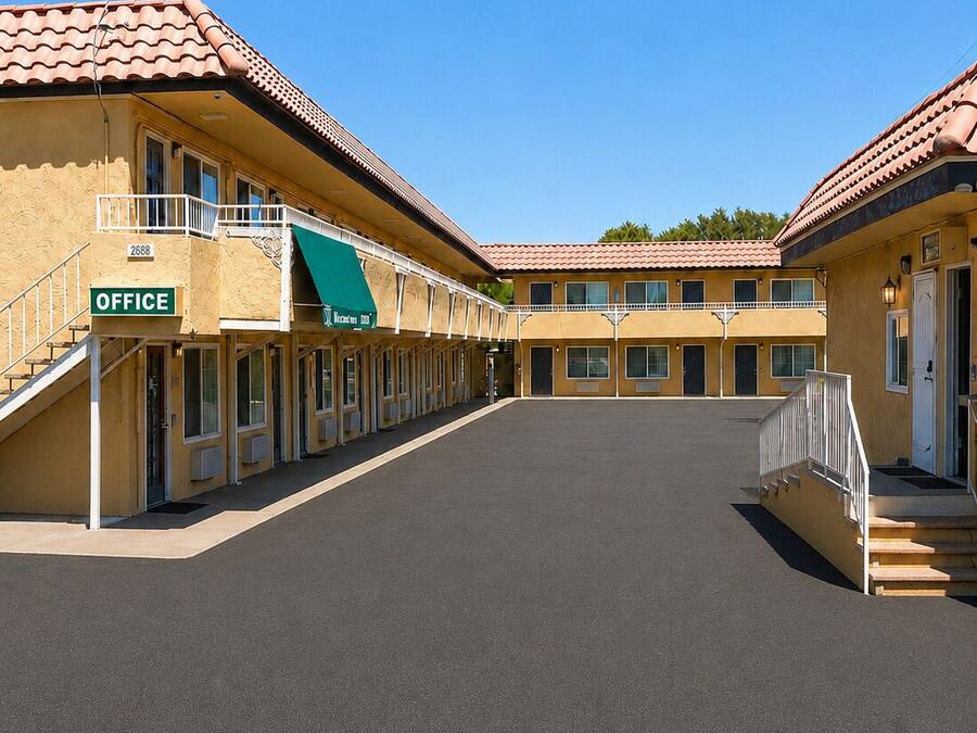 Un motel con un patio central, varias habitaciones con balcones y un letrero de la oficina.