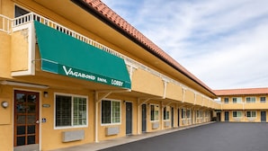 A hotel with a green awning labeled 'Vagabond Inn. Lobby,' multiple rooms with air conditioning units, and a clear sky. - Vagabond Inn Hemet (Hemet)