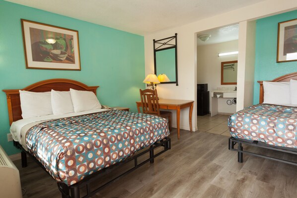 A hotel room with two beds, a desk, a chair, a lamp, and a bathroom visible through an open door.