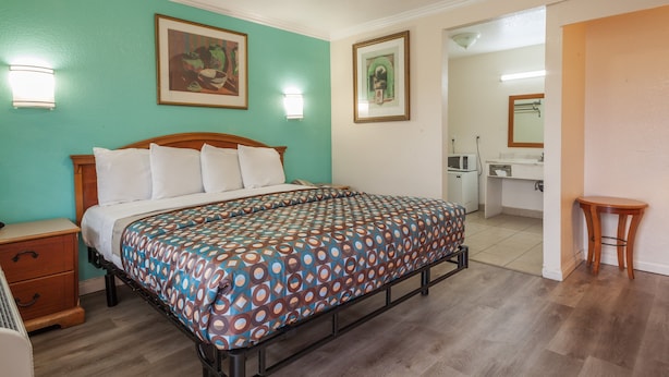 A bedroom with a bed, bedside tables, a dresser, a bathroom with a sink and mirror, and a small table. - Vagabond Inn Hemet (Hemet)