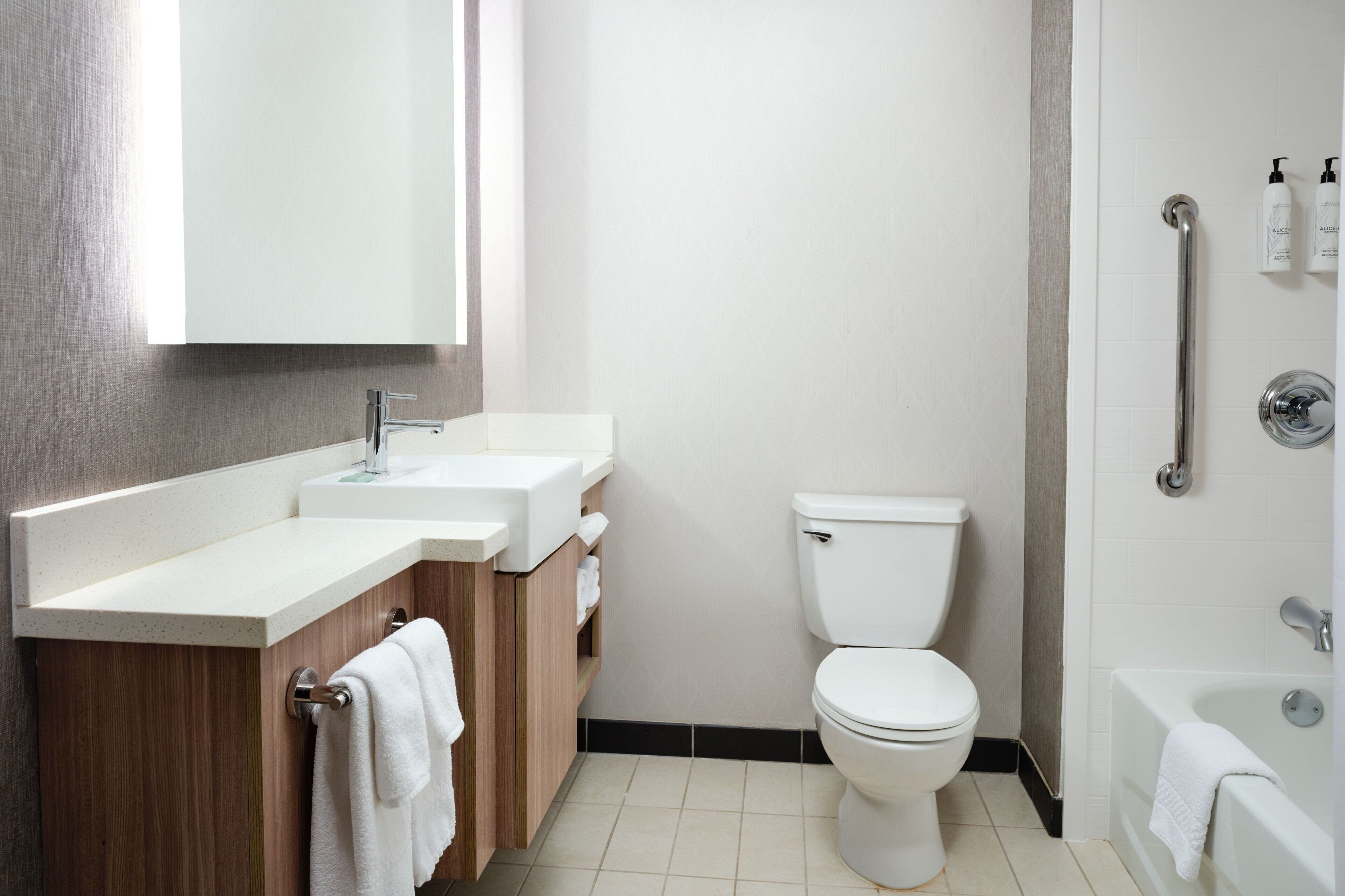 A modern bathroom with a white toilet, a sink with a wooden vanity, and a bathtub.