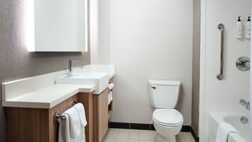 A modern bathroom with a white toilet, a sink with a wooden vanity, and a bathtub.