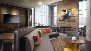 A modern lounge area with a sectional sofa, a yellow table, and a flat-screen TV mounted on the wall.