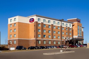 Un hôtel à plusieurs étages, doté d’une façade en briques, de nombreuses fenêtres et d’un parking où sont stationnées plusieurs voitures.