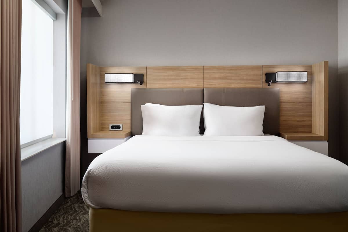 A hotel room with a large bed, two bedside tables, and a headboard with integrated lighting.