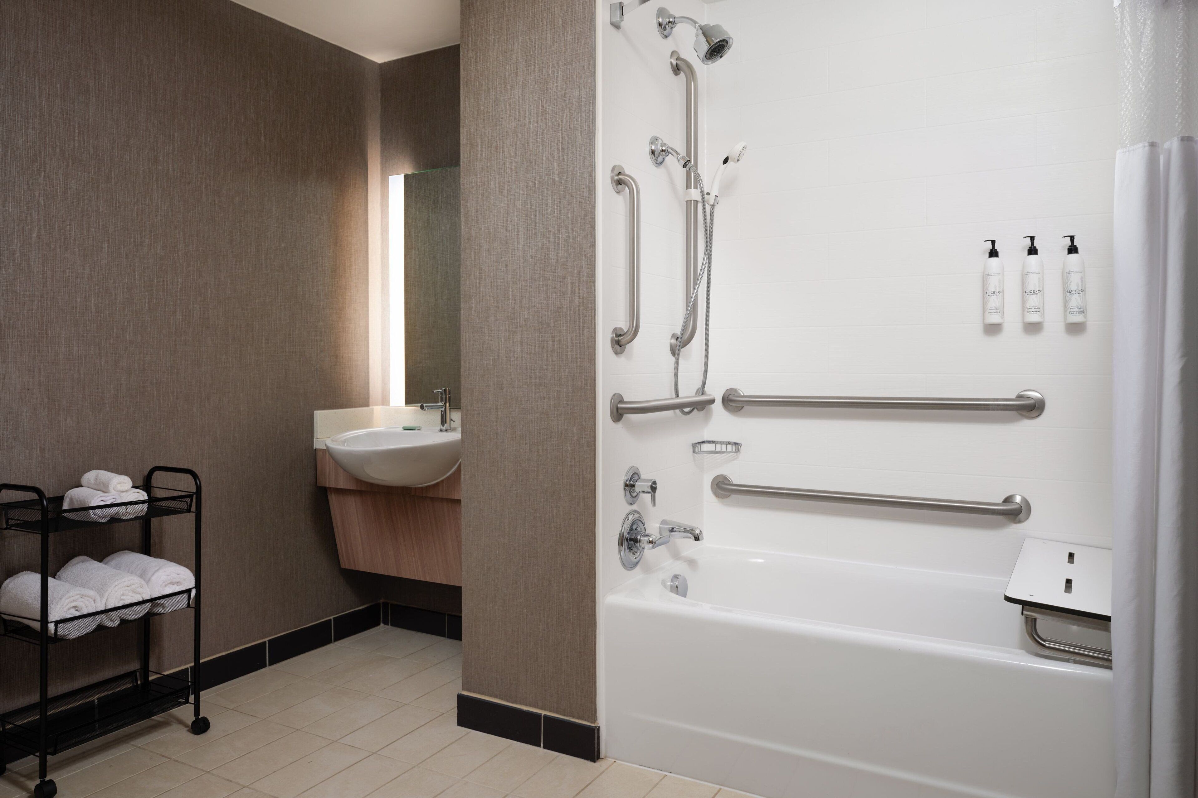 Une salle de bain moderne équipée d’une baignoire, de barres d’appui, d’un lavabo et d’un porte-serviettes.