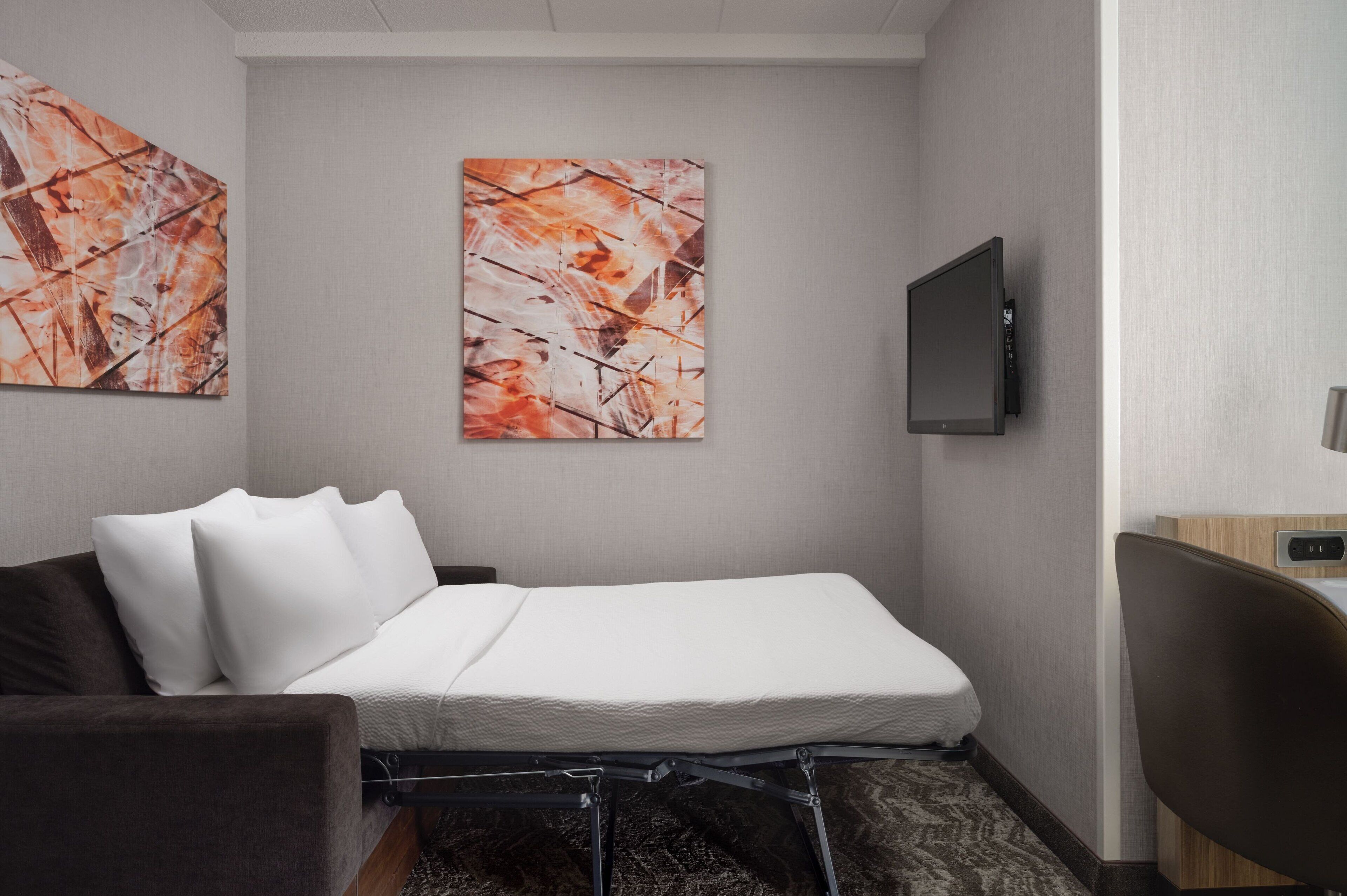 A hotel room with a bed, a TV mounted on the wall, and abstract artwork on the walls.