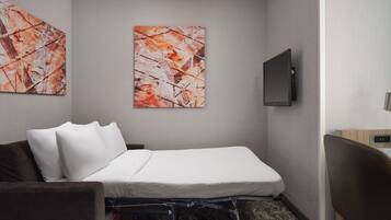 Quarto de hotel com uma cama, uma televisão na parede e obras de arte abstratas nas paredes.