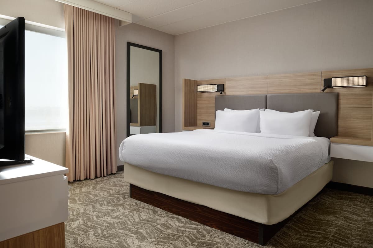 A hotel room with a large bed, a flat-screen TV, a mirror, and a window with curtains.