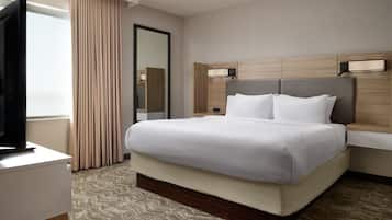 A hotel room with a large bed, a flat-screen TV, a mirror, and a window with curtains.