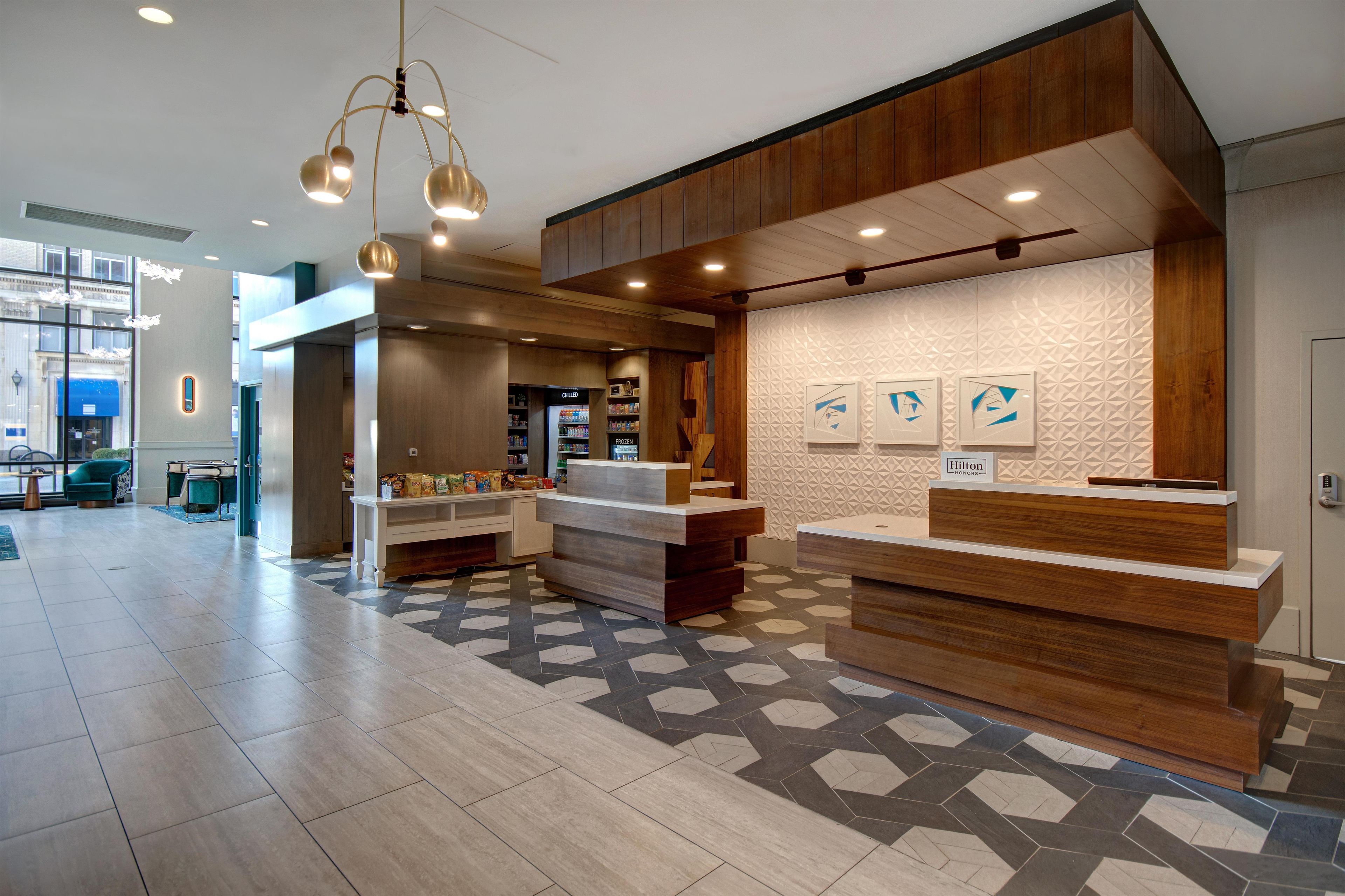 A hotel lobby with a reception desk, a seating area with a teal chair, and a food display.