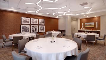 A conference room with round tables, chairs, framed pictures on the wall, and a carpeted floor.