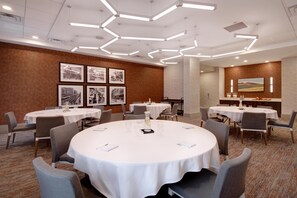 A conference room with round tables, chairs, framed pictures on the wall, and a carpeted floor.
