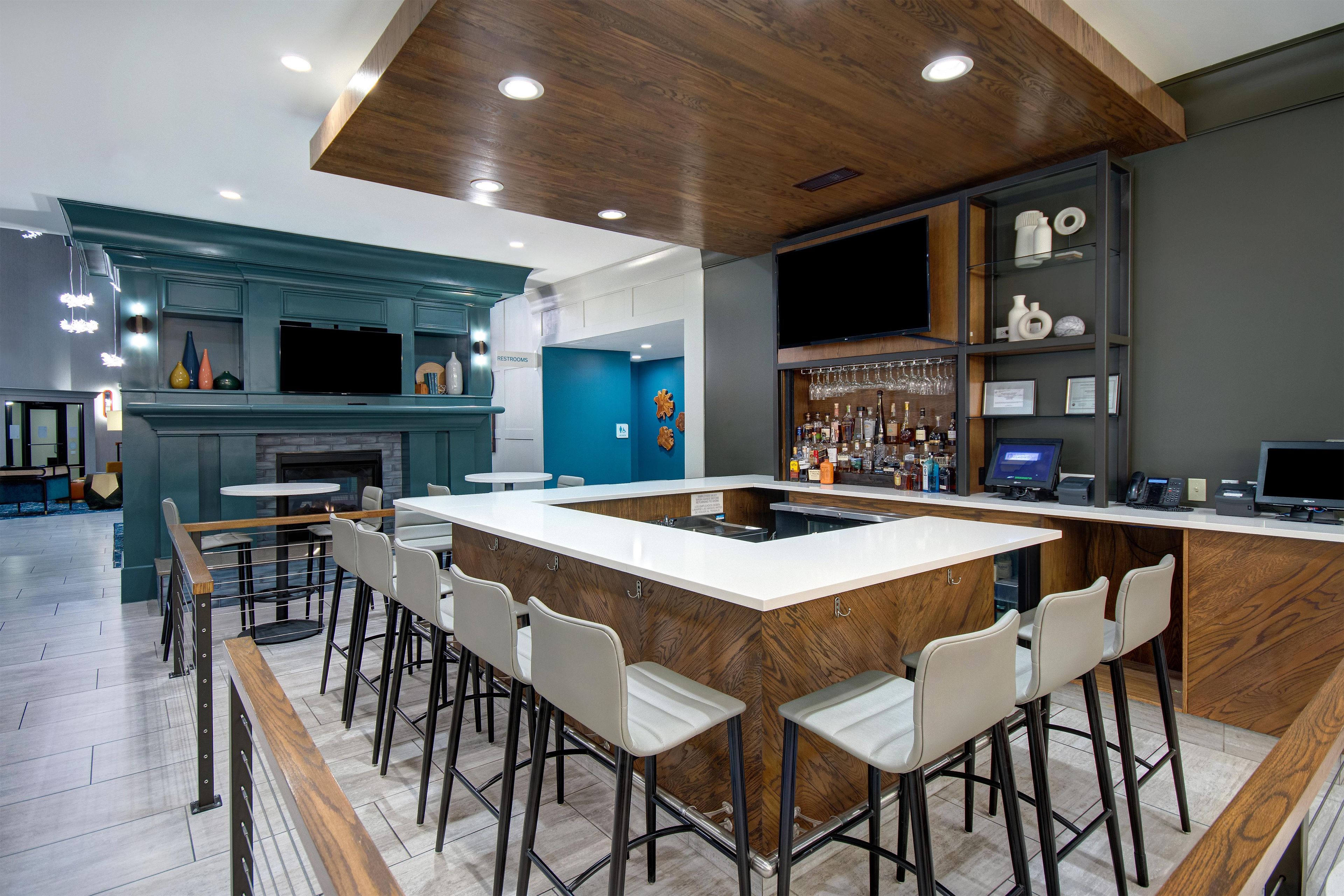 A modern bar area with a long counter, bar stools, and a television.