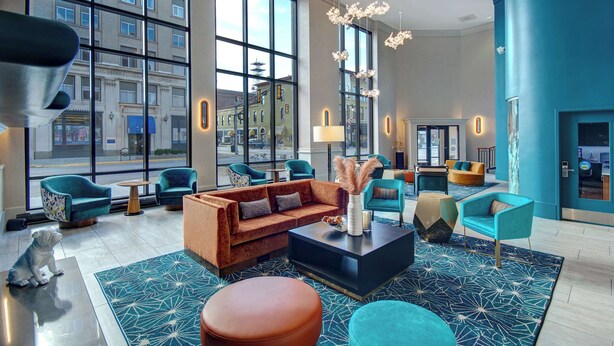 Un hall d’entrée moderne doté de grandes fenêtres, un espace de détente central avec des canapés et des fauteuils, ainsi qu’une table basse.