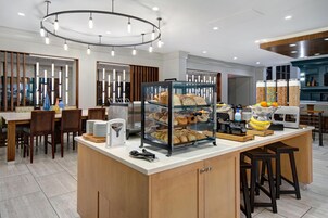 Un bufé de desayuno con diversas opciones de pastelería y pan, una máquina de café y un bol de fruta.