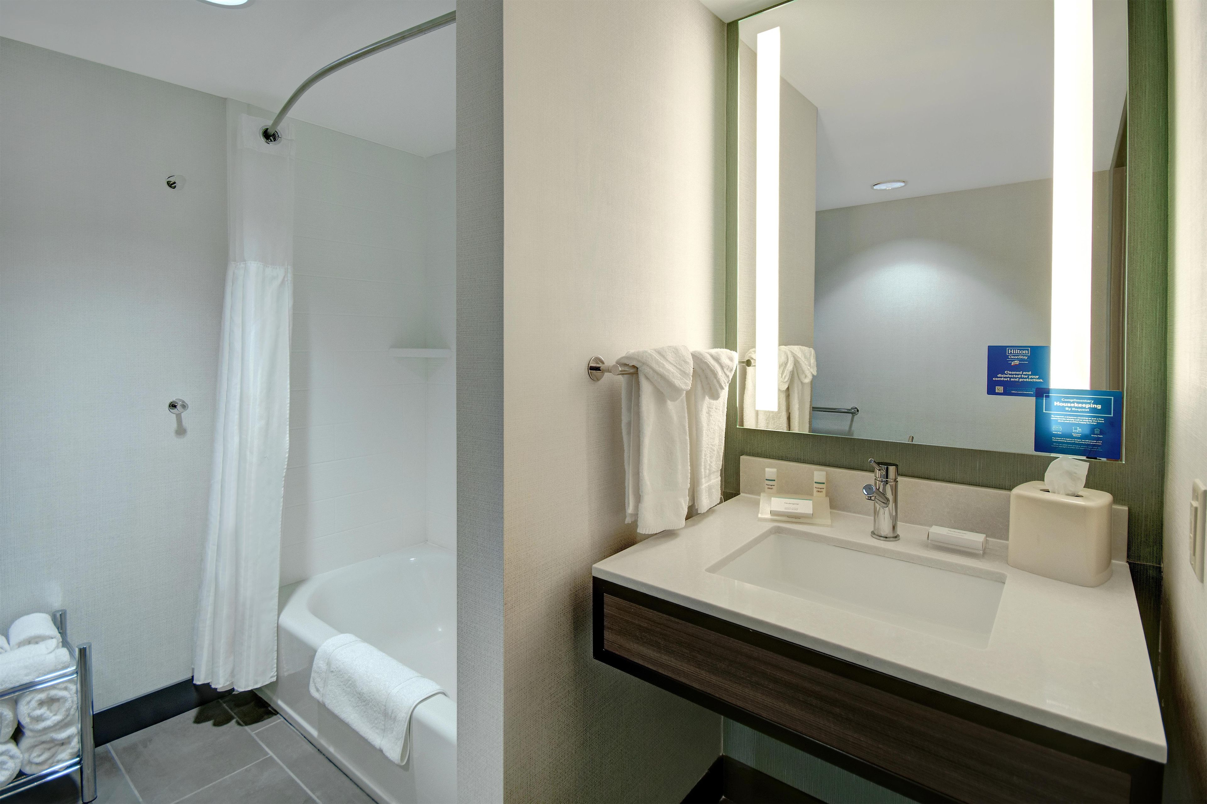 A hotel bathroom with a shower, a sink, and a mirror.